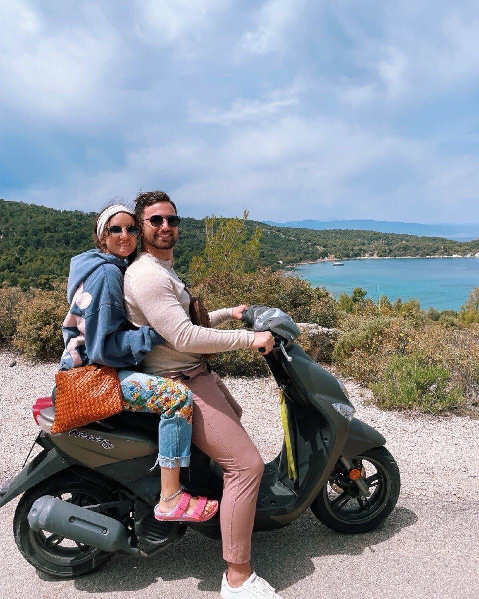 Dimitra Milan Dunn and Jake Dunn smiling as they ride mopeds on the island of Spetses, Greece