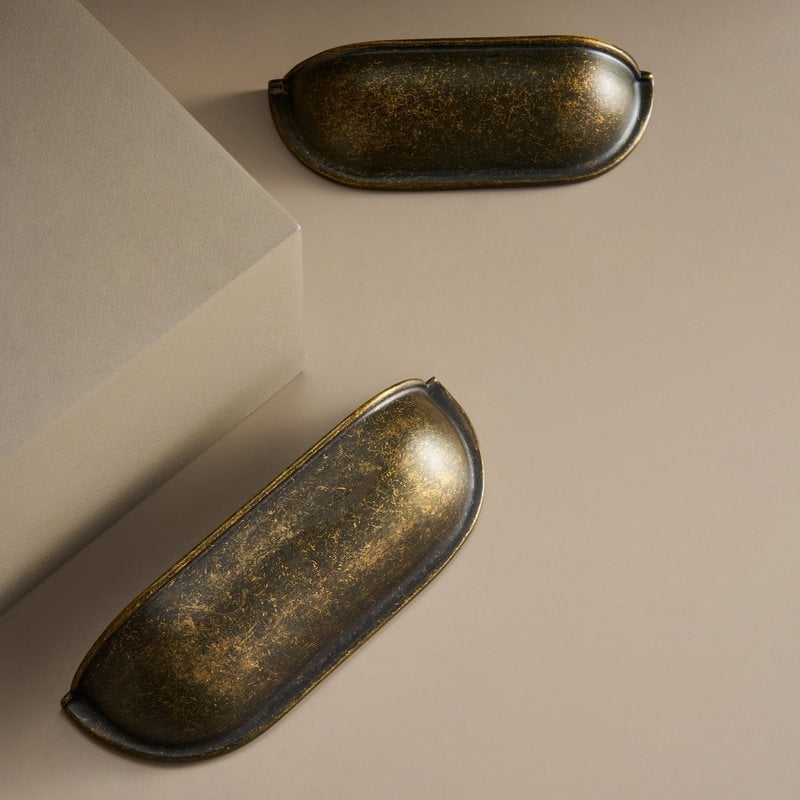 Two solid brass cup pulls in antique brass on a tan background